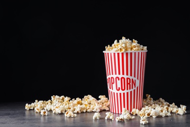 Bucket of fresh popcorn on grey stone table against black background, space for text. Cinema snack