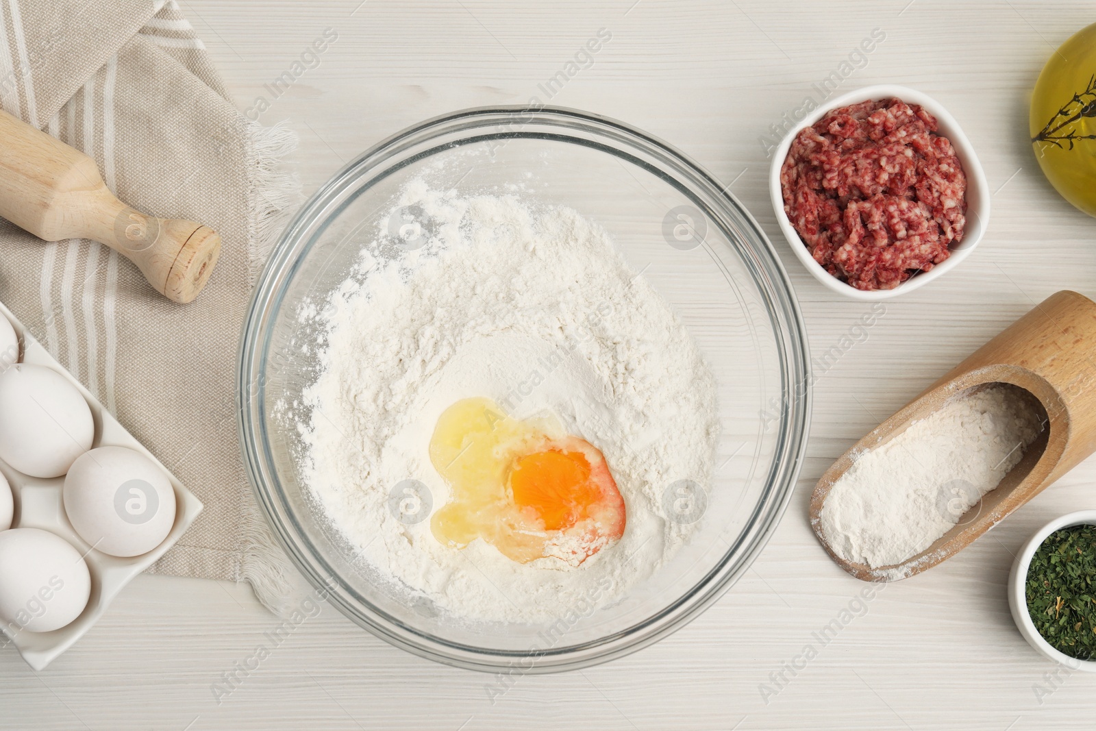 Photo of Bowl with flour, egg and products on white wooden table, flat lay