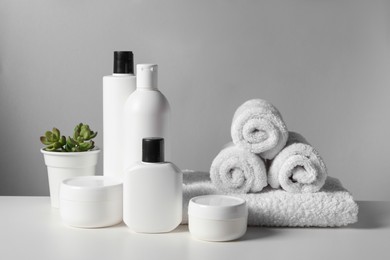 Photo of Different bath accessories, towels and houseplant on white table against grey background
