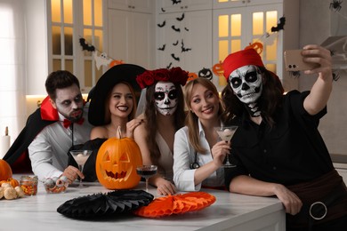 Group of people in scary costumes with cocktails taking selfie at Halloween party indoors
