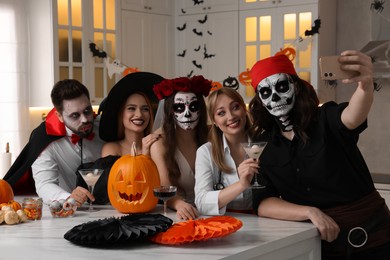 Photo of Group of people in scary costumes with cocktails taking selfie at Halloween party indoors