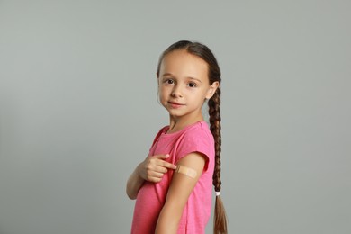 Vaccinated little girl showing medical plaster on her arm against light grey background