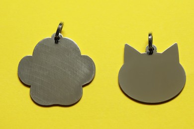 Silver pet tags on yellow background, flat lay. Space for text