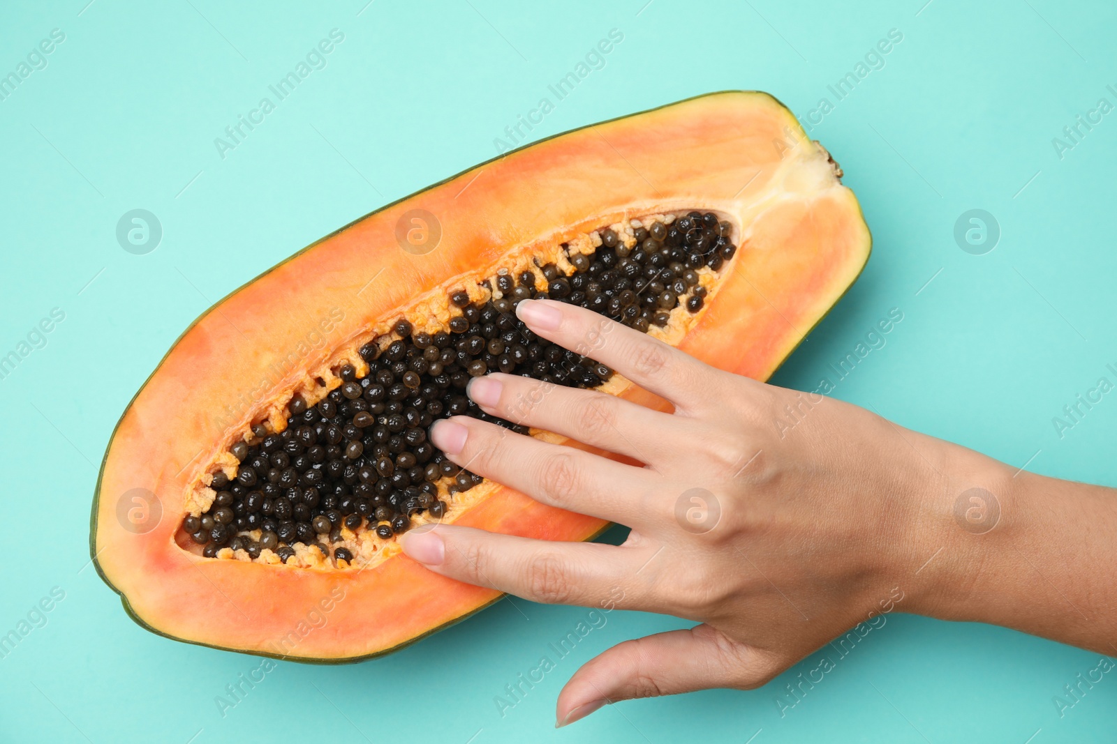 Photo of Young woman touching half of papaya on turquoise background, top view. Sex concept