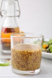 Photo of Tasty vinegar based sauce (Vinaigrette) in glass on light tiled table, closeup