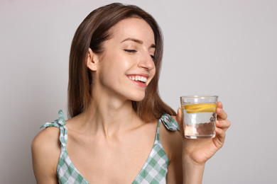 Young woman with glass of lemon water on light background