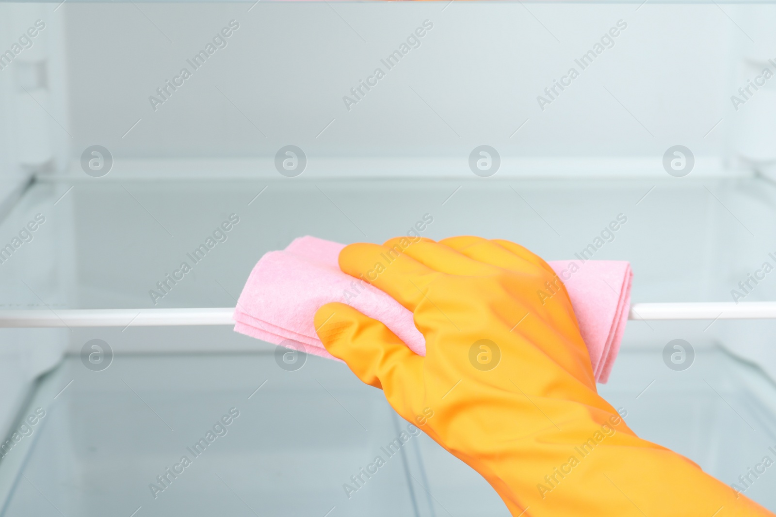 Photo of Woman cleaning empty refrigerator with rag, closeup