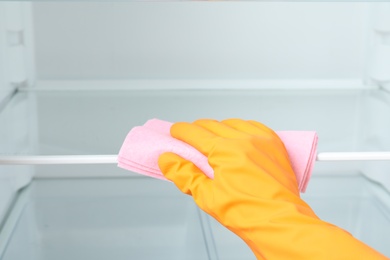 Woman cleaning empty refrigerator with rag, closeup