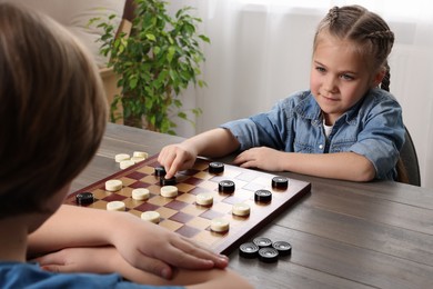 Photo of Cute boy playing checkers with little girl at table in room, closeup