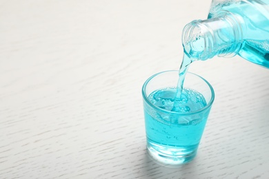 Photo of Pouring mouthwash in glass and space for text on wooden background. Teeth care