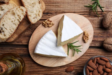 Photo of Tasty cut brie cheese with rosemary, bread and nuts on wooden table, flat lay