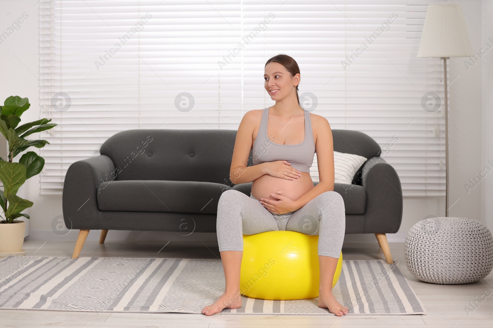 Photo of Pregnant woman sitting on fitness ball at home. Doing yoga