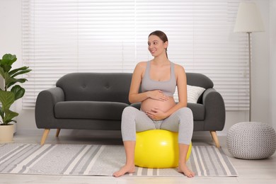 Pregnant woman sitting on fitness ball at home. Doing yoga