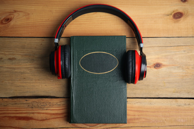Book and modern headphones on wooden table, top view