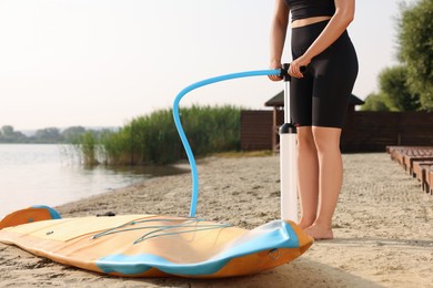 Photo of Woman pumping up SUP board on river shore, closeup