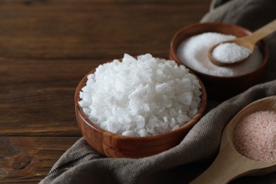 Photo of Different types of organic salt on wooden table, closeup