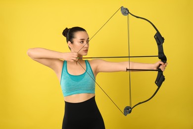 Photo of Sporty young woman practicing archery on yellow background