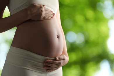 Young pregnant woman touching her belly outdoors, closeup. Space for text