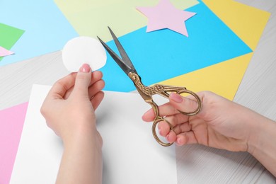 Woman holding paper circle and scissors at white wooden table, closeup