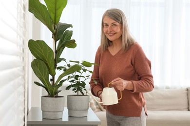 Photo of Senior woman watering beautiful potted houseplants at home