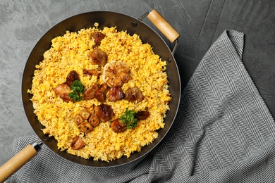 Photo of Frying pan with delicious rice pilaf and napkin on grey background, top view