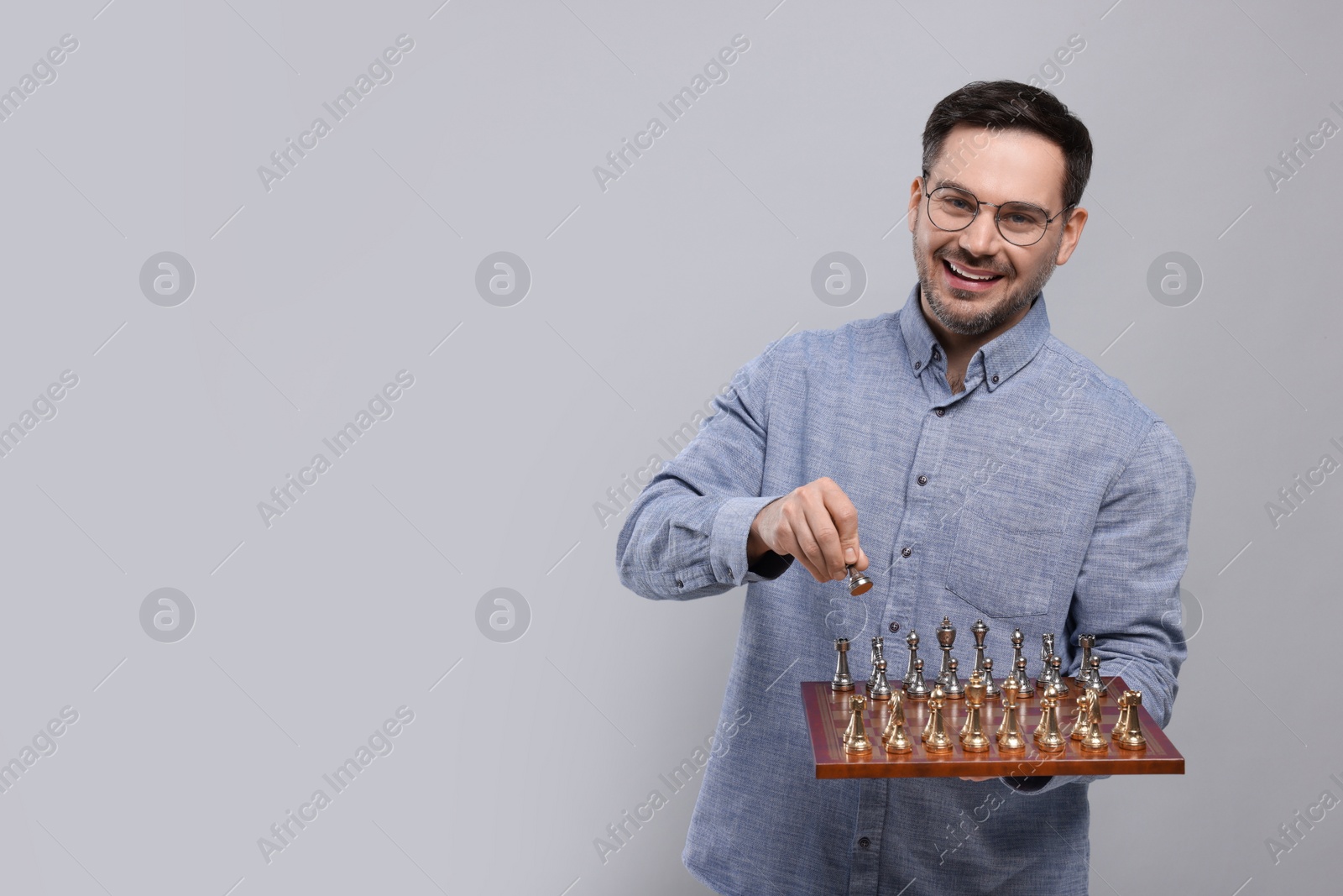 Photo of Smiling man holding chessboard with game pieces on light grey background, space for text