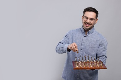 Photo of Smiling man holding chessboard with game pieces on light grey background, space for text