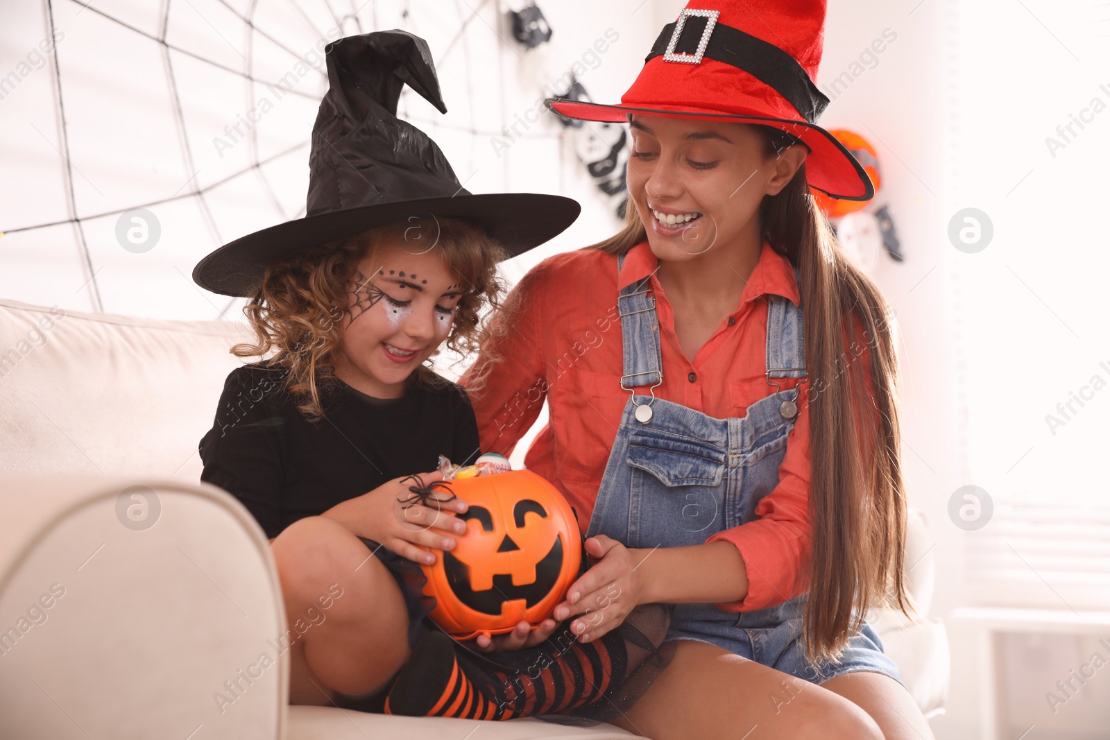 Photo of Mother and cute little girl with pumpkin candy bucket in Halloween costumes at home