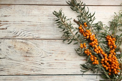 Branches of sea buckthorn on white wooden table, flat lay. Space for text