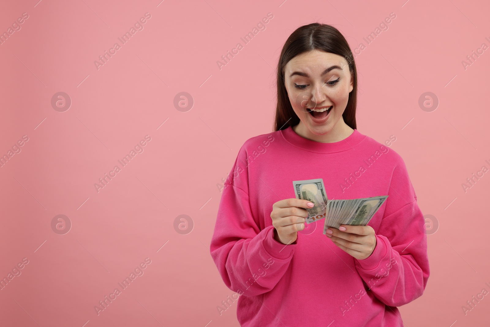 Photo of Excited woman with dollar banknotes on pink background, space for text