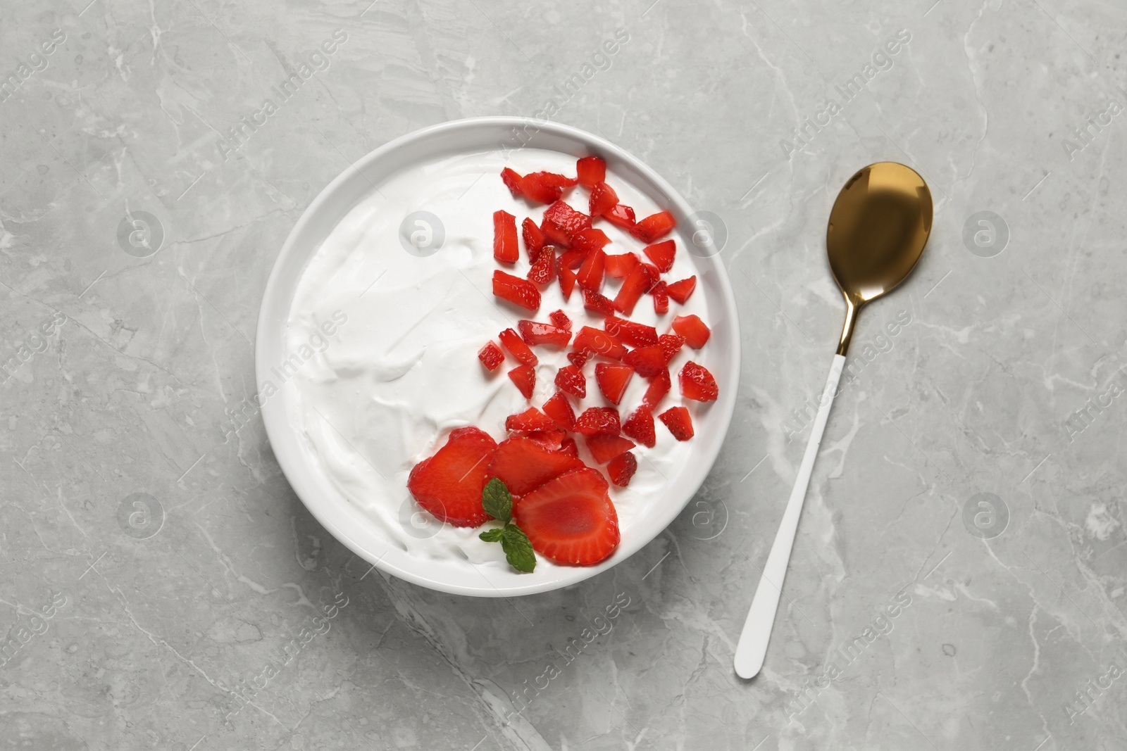 Photo of Delicious yogurt with strawberries served on grey marble table, top view
