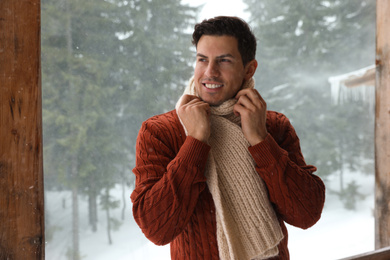 Photo of Handsome man wearing warm sweater and scarf outdoors on snowy day. Winter season