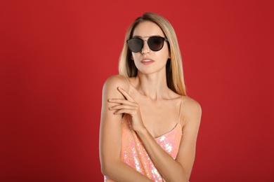 Beautiful woman in stylish sunglasses on red background