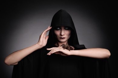 Mysterious witch with spooky spider on dark background
