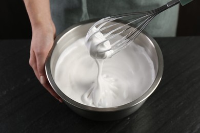 Photo of Woman making whipped cream with whisk at black table, closeup