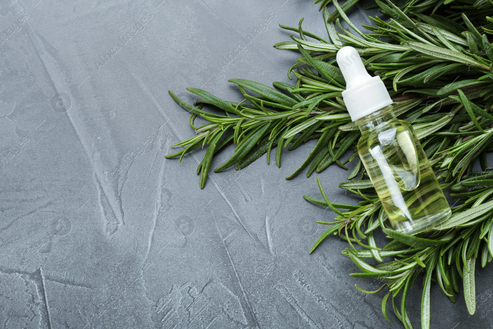 Photo of Fresh rosemary and bottle of essential oil on grey table, flat lay. Space for text