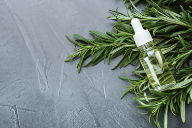 Fresh rosemary and bottle of essential oil on grey table, flat lay. Space for text