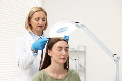 Trichologist examining patient`s hair under lamp in clinic