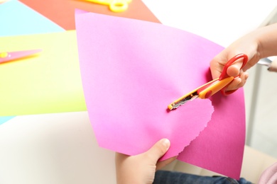 Photo of Child cutting out paper heart with craft scissors at table, closeup. Space for text