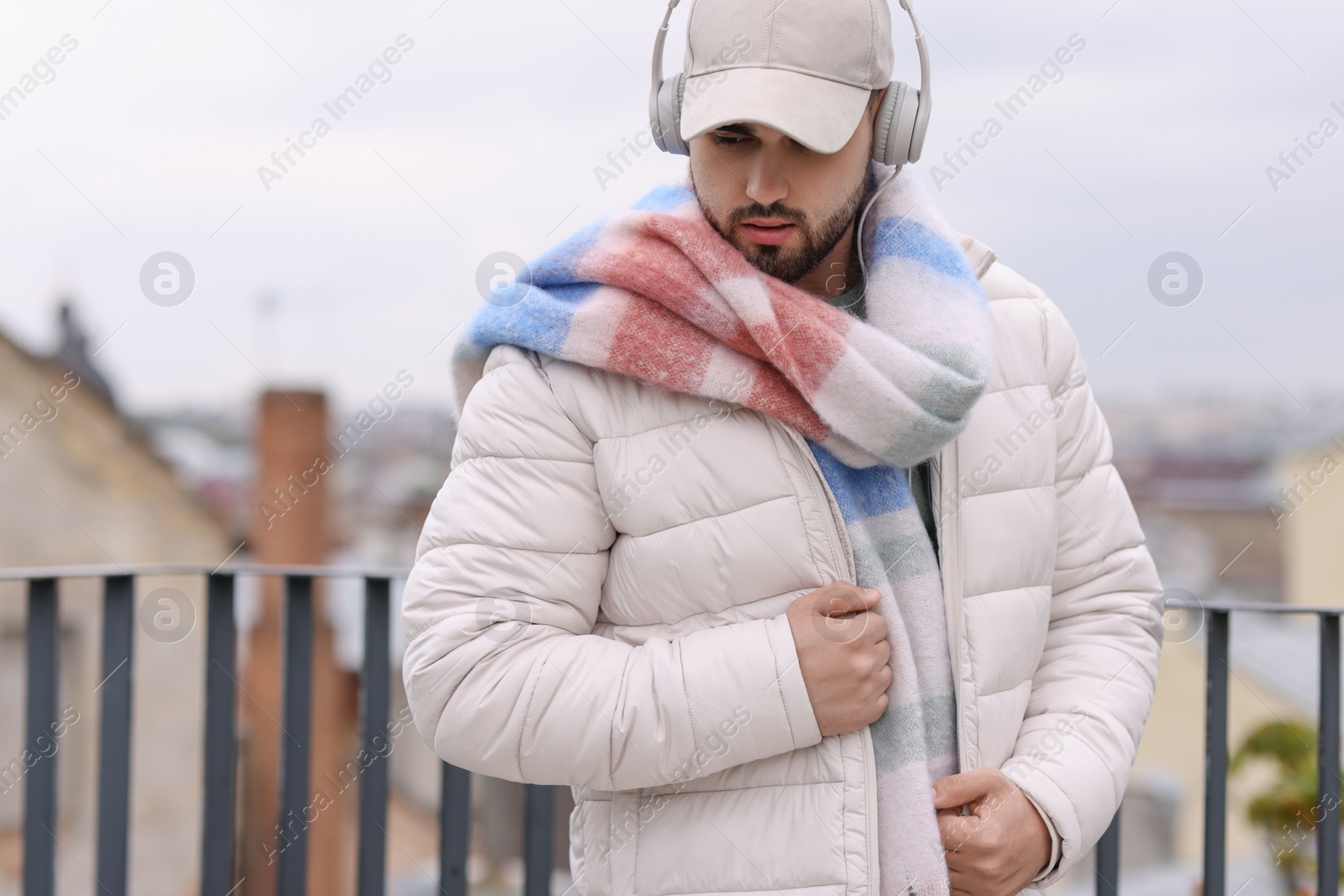 Photo of Handsome man in warm scarf and headphones outdoors