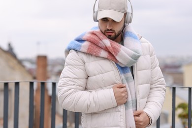 Handsome man in warm scarf and headphones outdoors