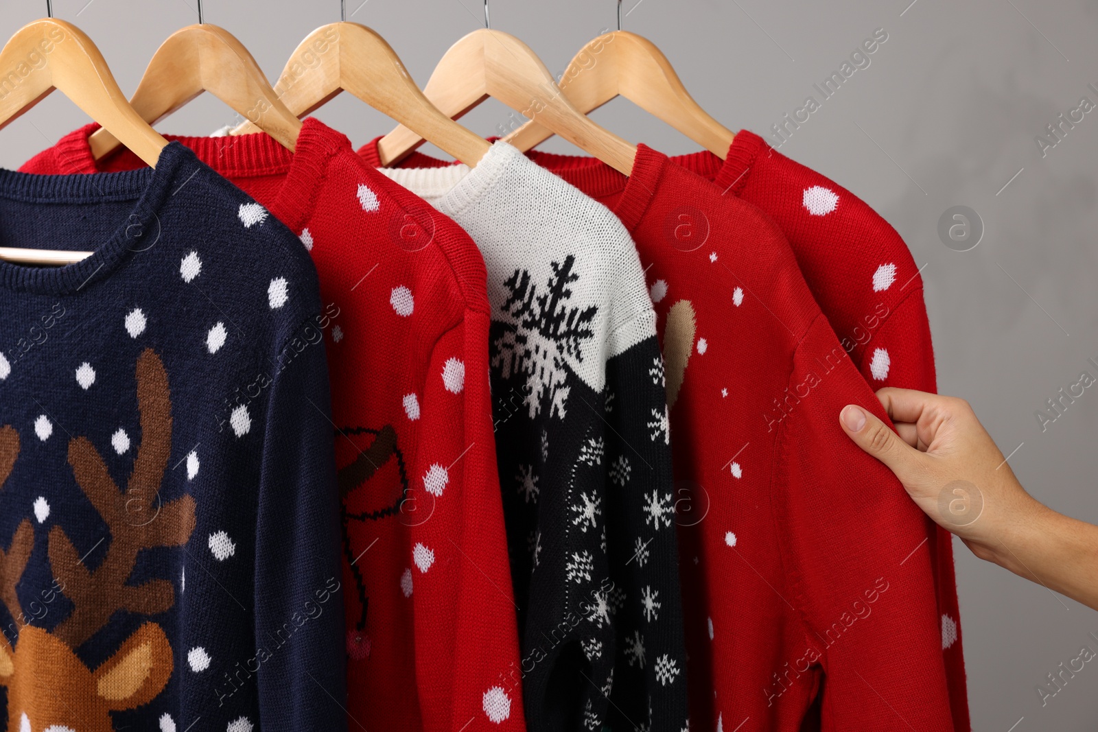 Photo of Woman choosing Christmas sweater from rack near light wall, closeup