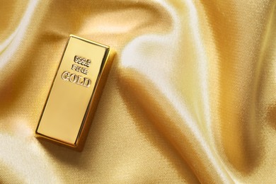 Photo of Gold bar on shiny silk fabric, top view. Space for text