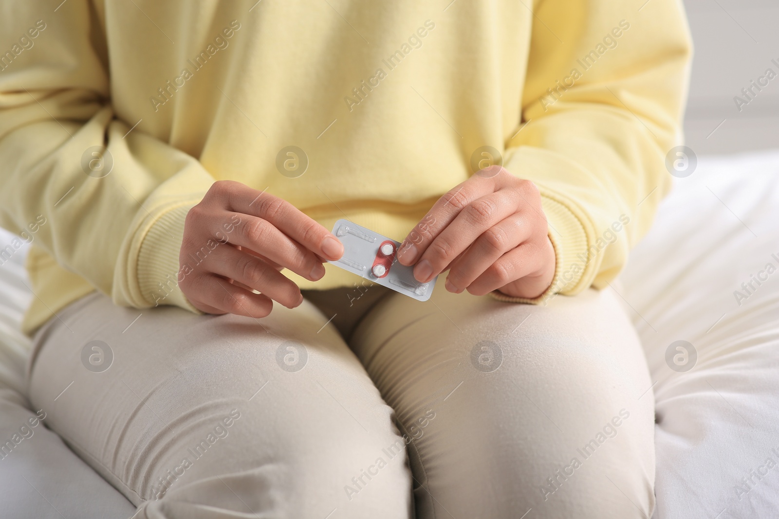 Photo of Woman holding blister of emergency contraception pills in bedroom, closeup