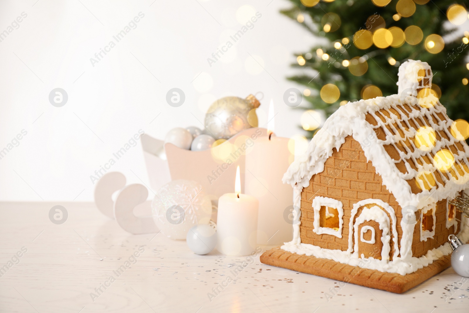 Photo of Beautiful gingerbread house decorated with icing and candles on white table