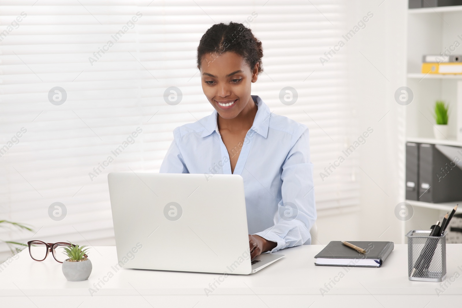 Photo of Smiling African American intern working on laptop at white table in office