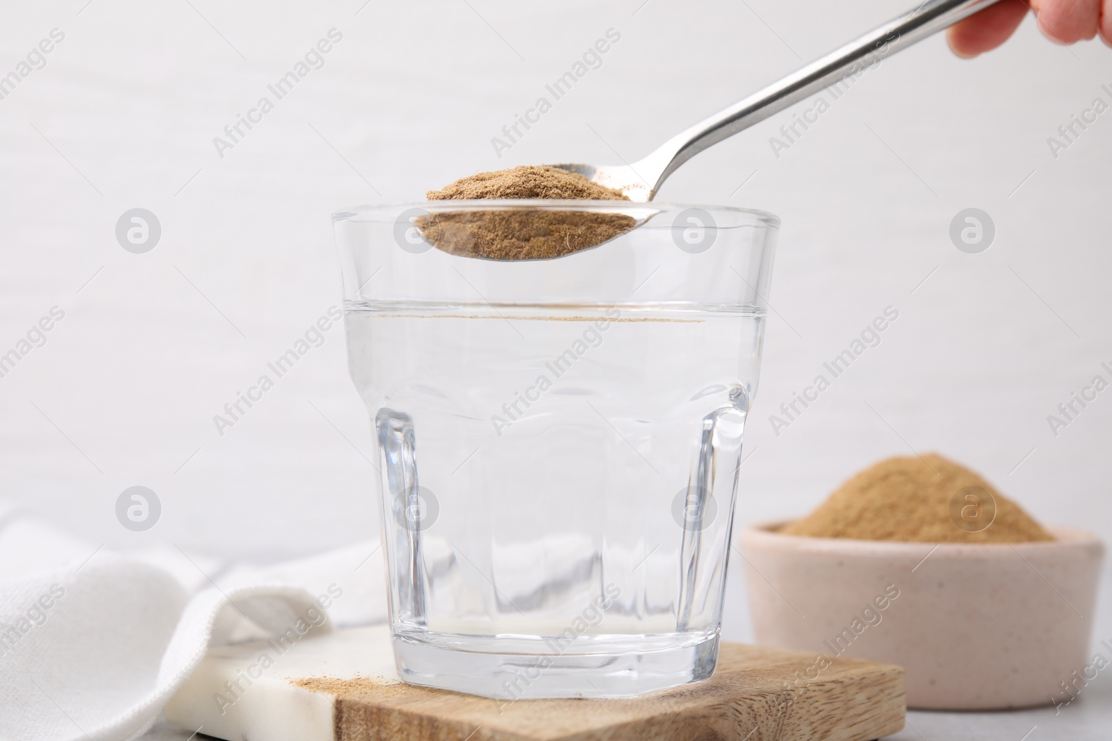 Photo of Dietary fiber. Woman adding psyllium husk powder into water at table, closeup
