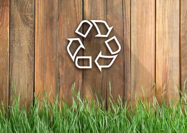 Green grass and illustration of recycling symbol on wooden fence