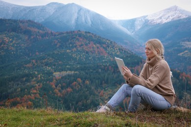 Young woman drawing on tablet in mountains, space for text