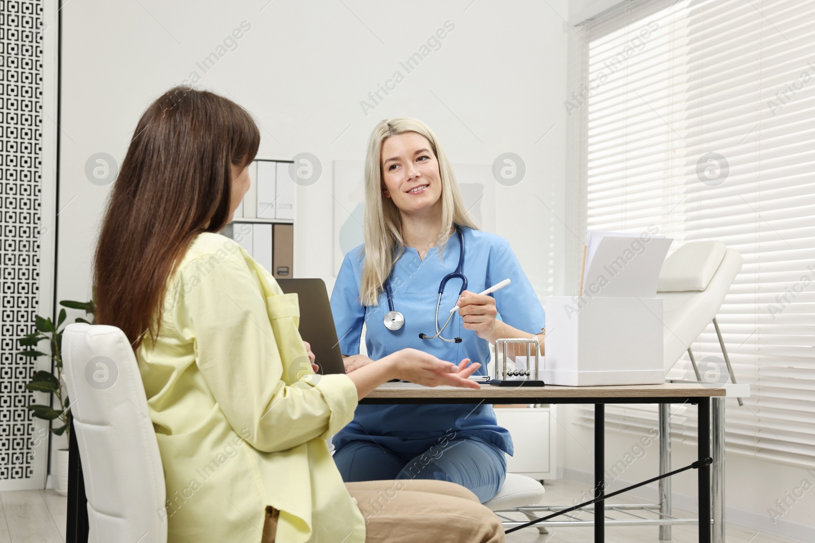 Photo of Smiling doctor consulting pregnant patient at table in clinic